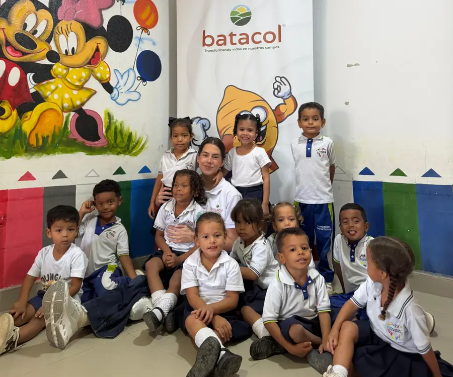 Niños y niñas con uniforme de la Fundación Dar y Darse junto a una integrante del equipo Batacol, frente al pendón de Batacol